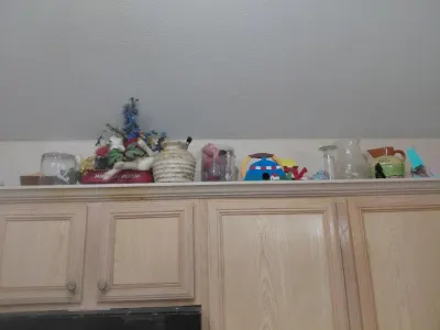 Decorative items on top of kitchen cabinets: faux flowers, birdhouse, glass pitchers, jars
