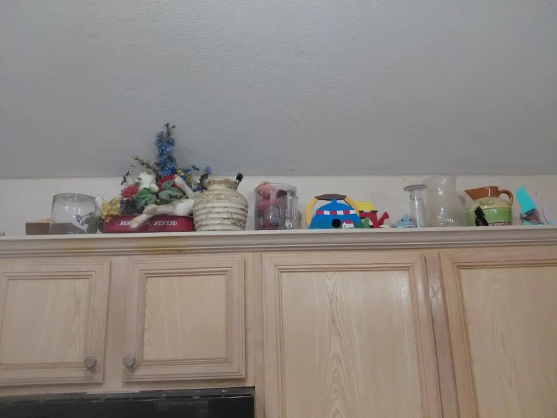 Decorative items on top of kitchen cabinets: faux flowers, birdhouse, glass pitchers, jars