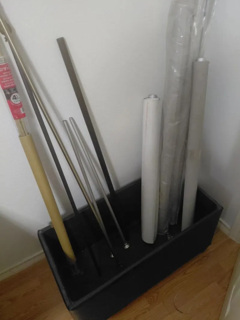 Curtain rods, metal poles and rolled window shades in a black storage bin