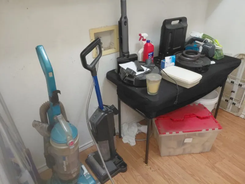 Upright vacuum cleaners, cordless stick vacuum and black folding table with household items