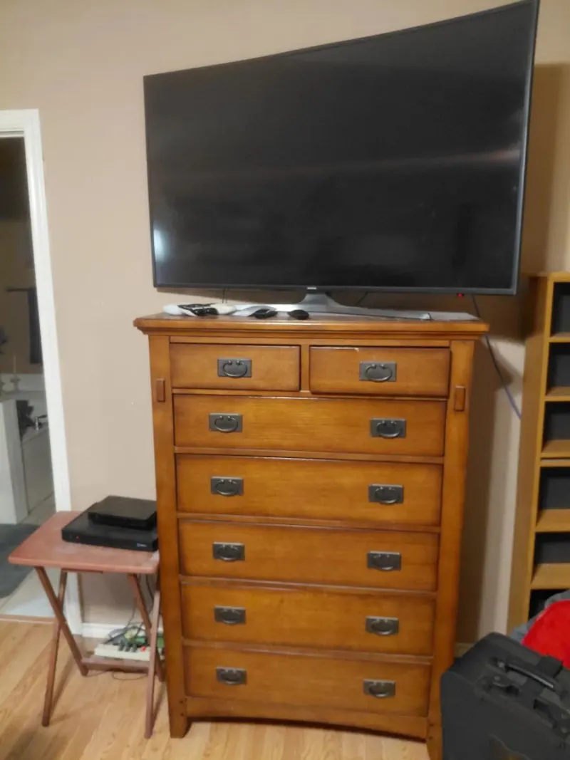 Mission style oak tall chest of drawers with curved flat screen TV