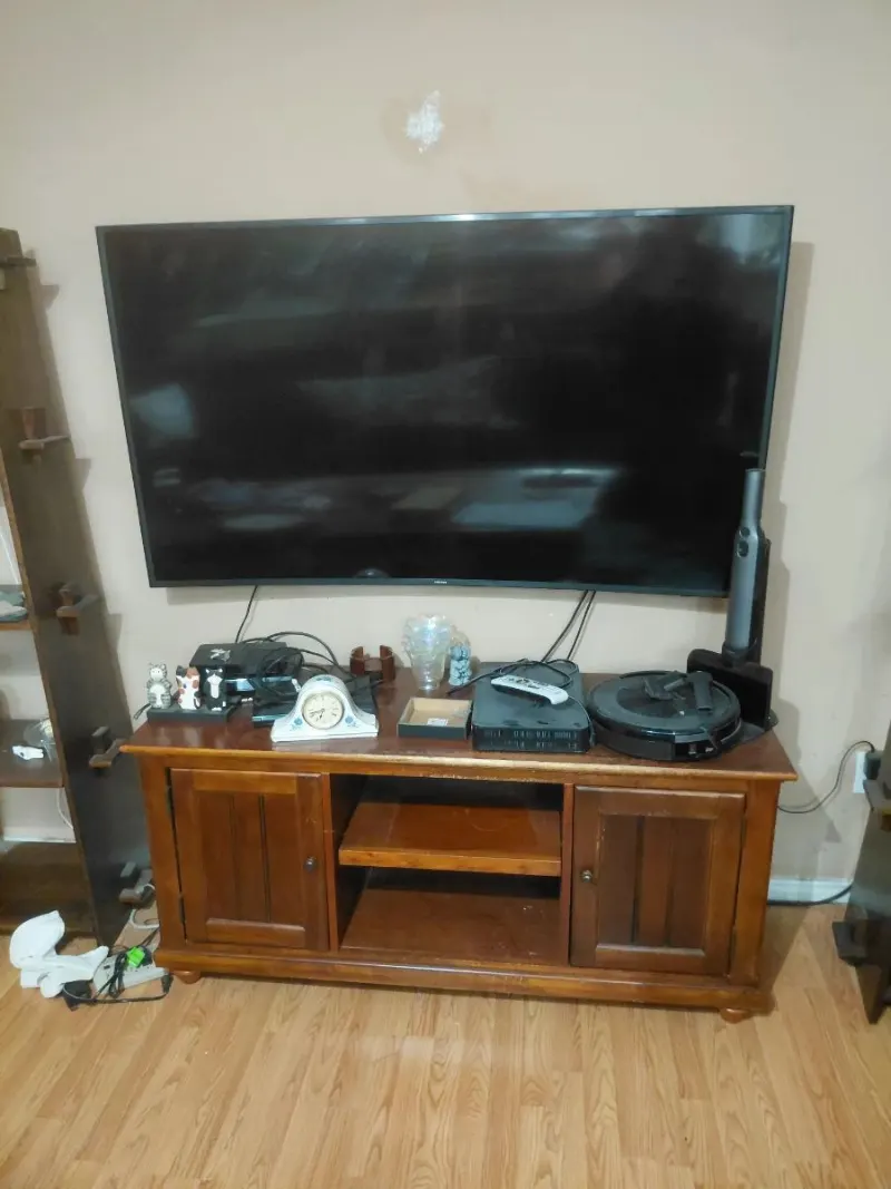 Wall-mounted flat screen TV and wood TV stand with cabinets, robot vacuum, clock